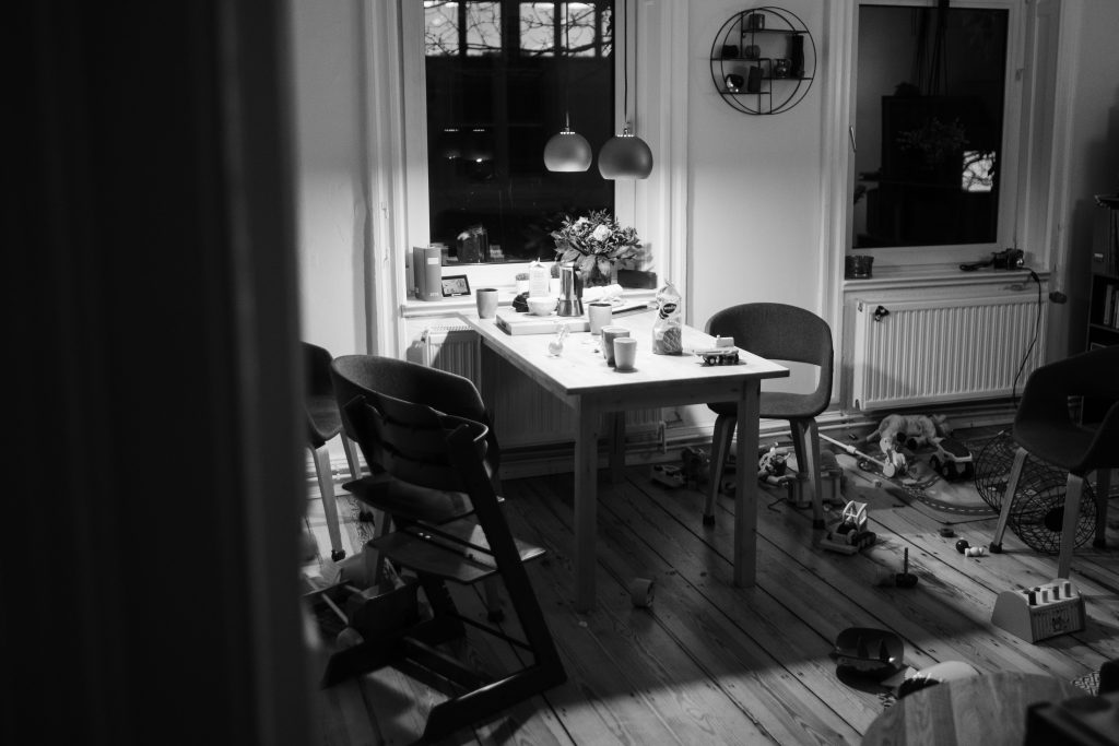 auf einem Küchentisch stehen Tassen & Kekse, über dem Tisch hängen 2 runde Deckenlampen, um den Tisch herum liegen einige Spielzeuge auf dem Boden verteilt