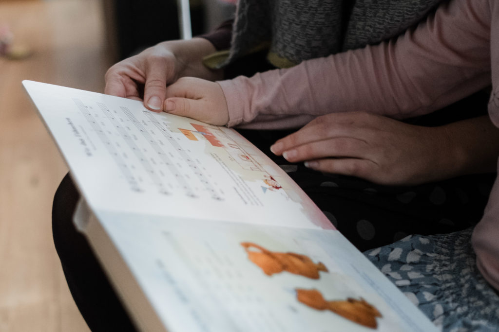 ein aufgeschlagenes Kinderbuch in den Händen einer Muter und eines Mädchens