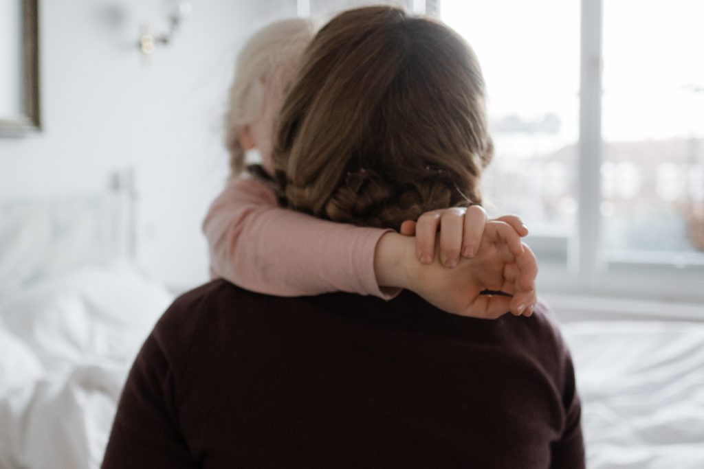 eine Mutter hat ihre Tochter auf den Arm, die Tochter hält ihre Hände um den Hals der Mutter