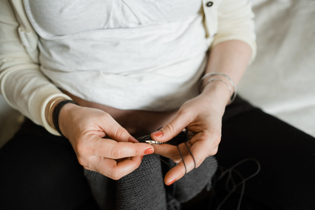 eine schwangere Frau sitzt auf einem Sofa, sie strickt