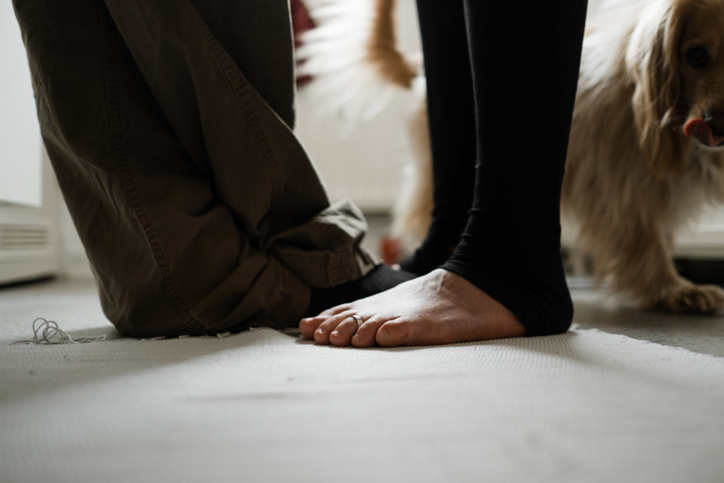 in einer Küche stehen ein Mann und eine Frau sich gegenüber, die Frau ist Barfuß, der Mann trägt Socken, seitlich von ihnen steht ein Hund