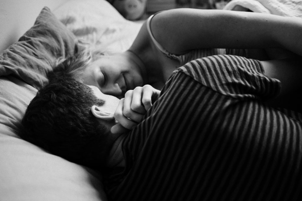 ein Mann und eine Frau liegen in einem Bett im Schlafzimmer, ihre Gesichter sind zueinander gerichtet, sie schließt ihre Augen