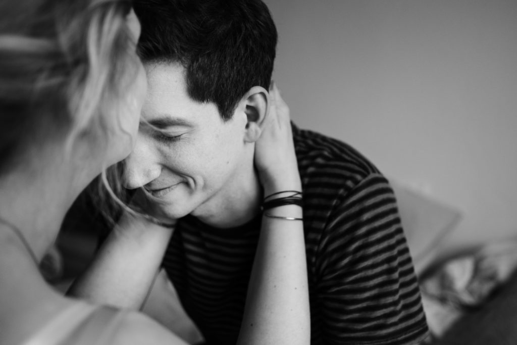 eine Frau legt ihre Hände um den Nacken des Mannes, sie küsst seine Stirn, der Mann schließt seine Augen