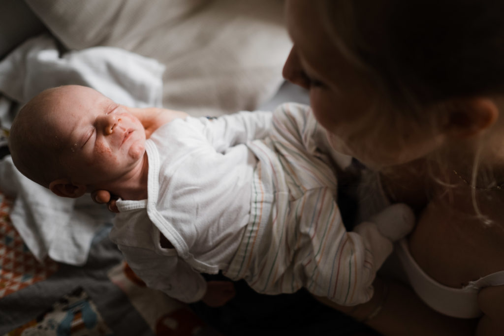 eine Frau hält ihr Baby in den Händen, sie schaut auf das Baby, das Baby hat geschlossene Augen