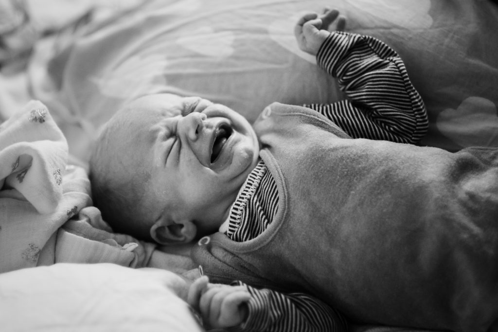 ein Baby liegt auf einer Wickeldecke auf einem Sofa, das Baby weint