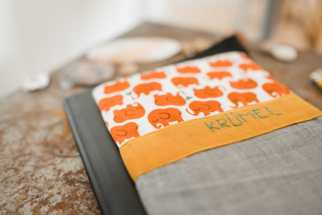 auf einem Tisch liegt ein Buch, dass mit einem Einband gebunden ist, auf dem Einband sind orangene Elefanten zu sehen, 