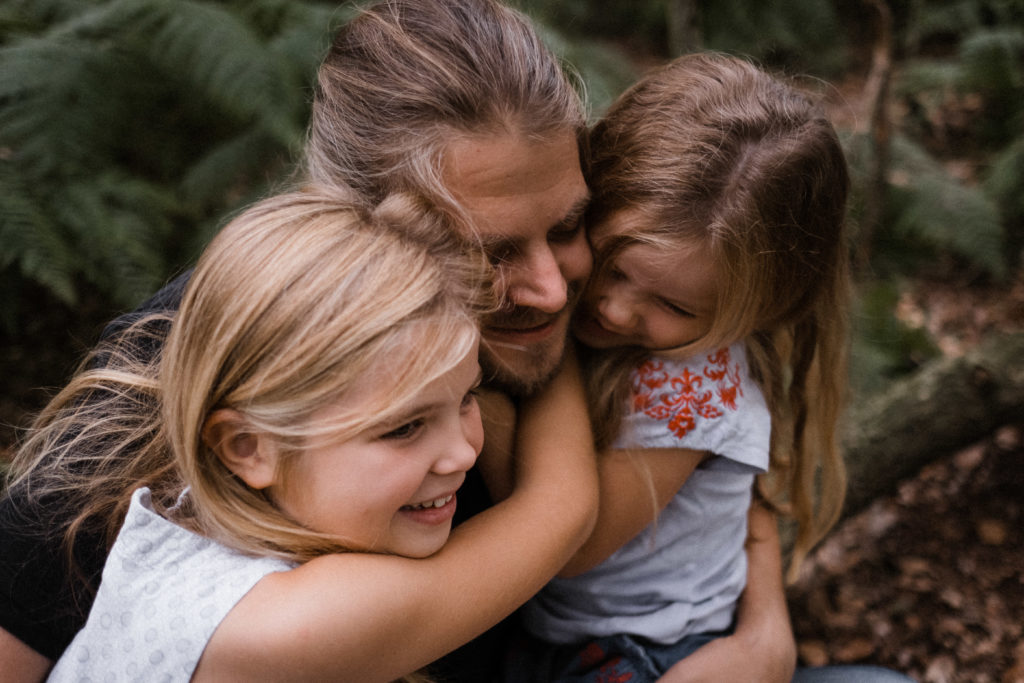 2 Töchter umarmen ihren Vater, ihre Köpfe halten sie aneinander
