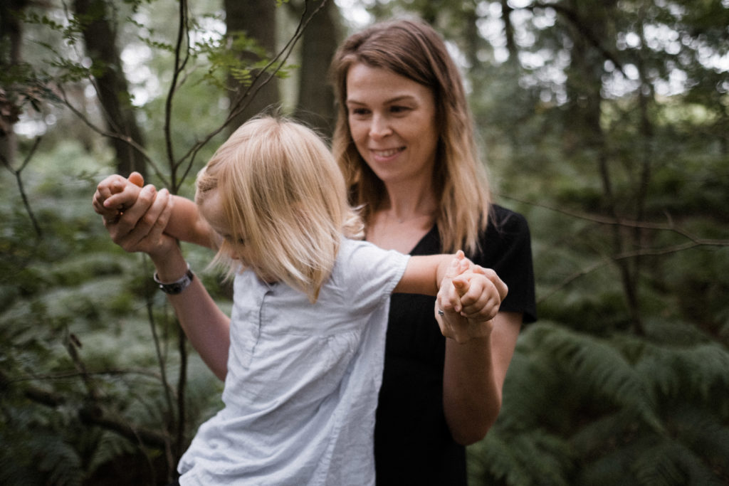 eine Mutter hält ihre kleine Tochter an den Armen fest, sie sind in einem Wald