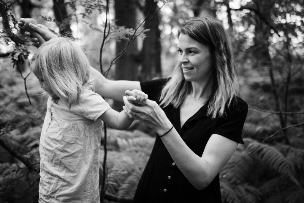 eine Mutter hält ihre kleine Tochter an den Armen fest, sie sind in einem Wald