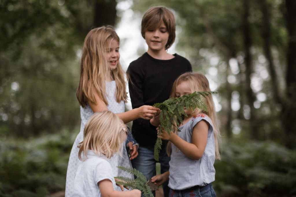 ein Junge steht mit seinen 3 Schwestern in einem Wald, ein Mädchen hält einen Fahn in der Hand