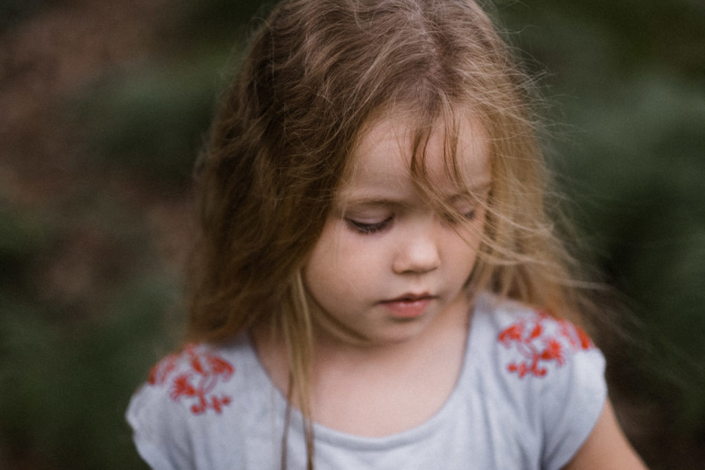 einem Mädchen wehen ihre langen Haare ins Gesicht, sie schaut nach unten