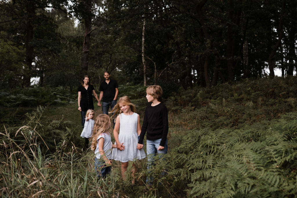 an der Lichtung in einem Wald steht eine Mutter und ein Vater mit ihren 3 Töchtern und einem Sohn, 2 der Töchter und der Sohn halten sich an der Hand, sie stehen im Vordergrund