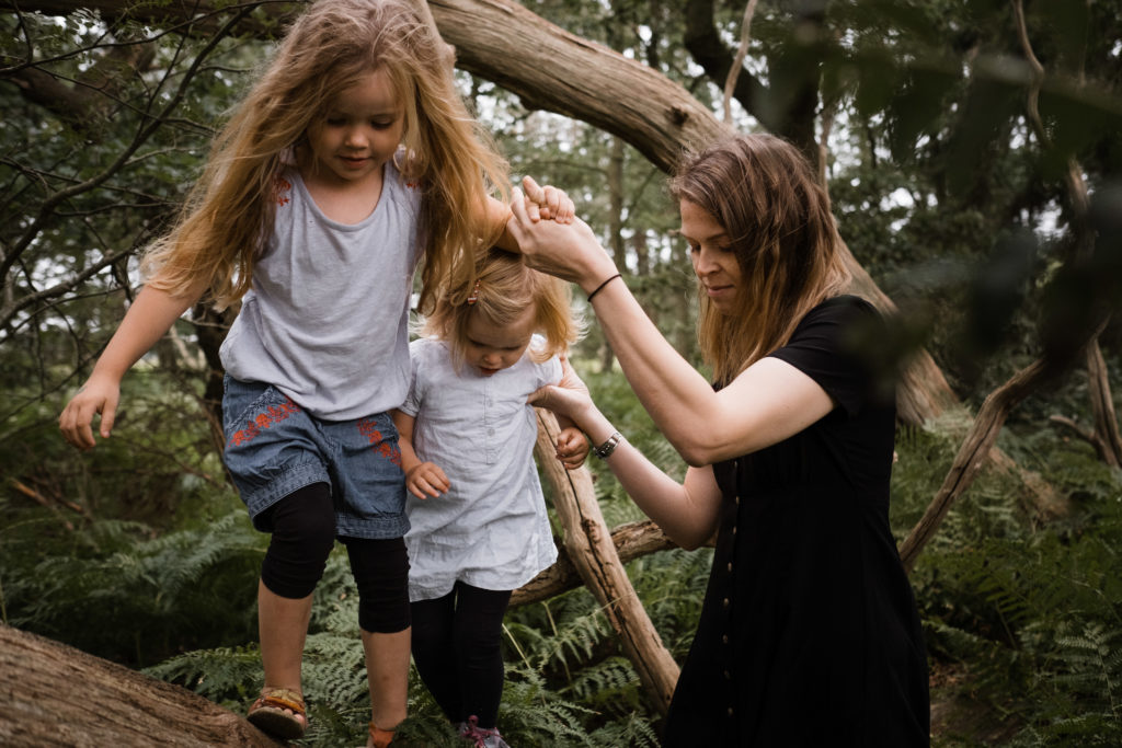 im Wald balancieren 2 Mädchen auf einem Baumstamm, ihre Mutter hält ihre Hände