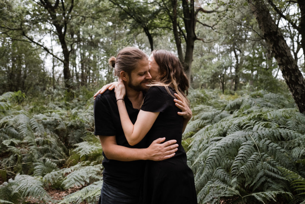 im Wald stehen eine Mutter und ein Vater, sie umarmen sich, um sie herum ist großer Fahn