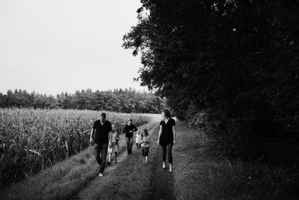 eine Mutter und ein Vater gehen mit ihren 3 Töchtern und ihrem Sohn entlang eines Waldrandes