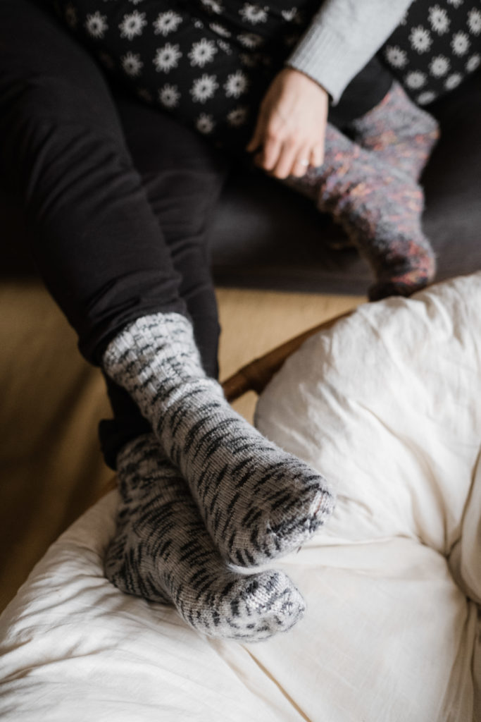 2 Frauen liegen auf einem Sofa, sie haben beide Wollstricksocken an