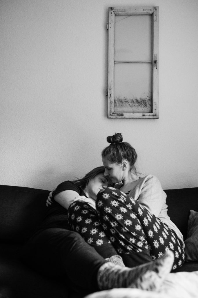 2 Frauen sitzen auf einem Sofa, sie halten ihre Köpfe aneinander und umarmen sich