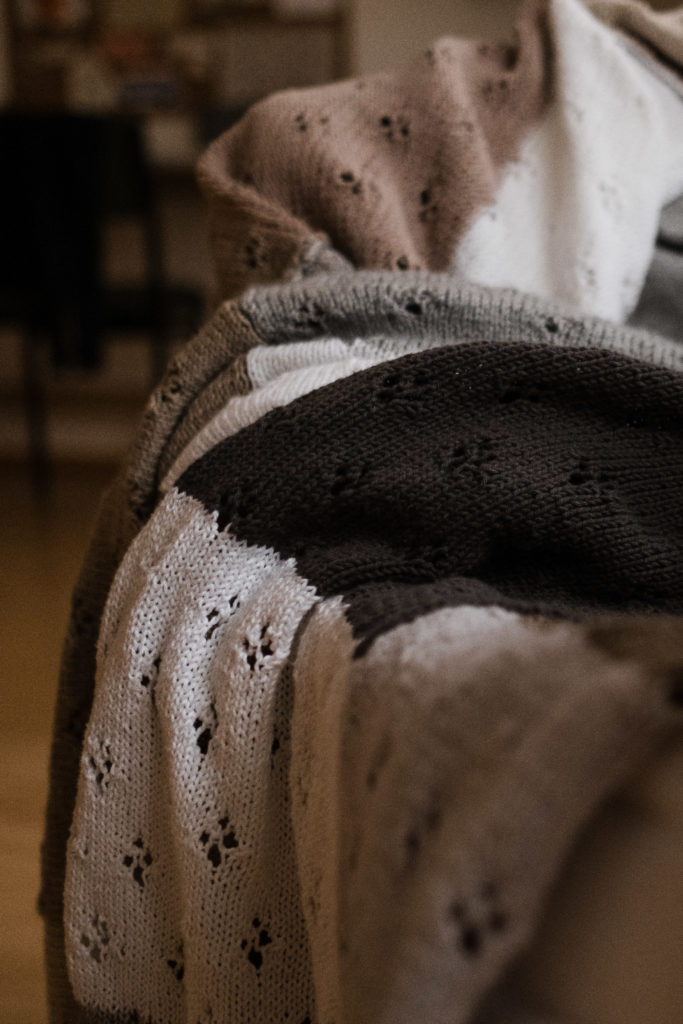 eine gestrichte Woldecke liegt auf einem Sessel, sie ist in Naturtönen gehalten