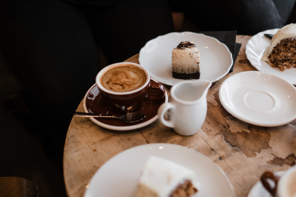 auf einem alten, runden Holztisch stehen Kaffeetassen und Teller mit Torte