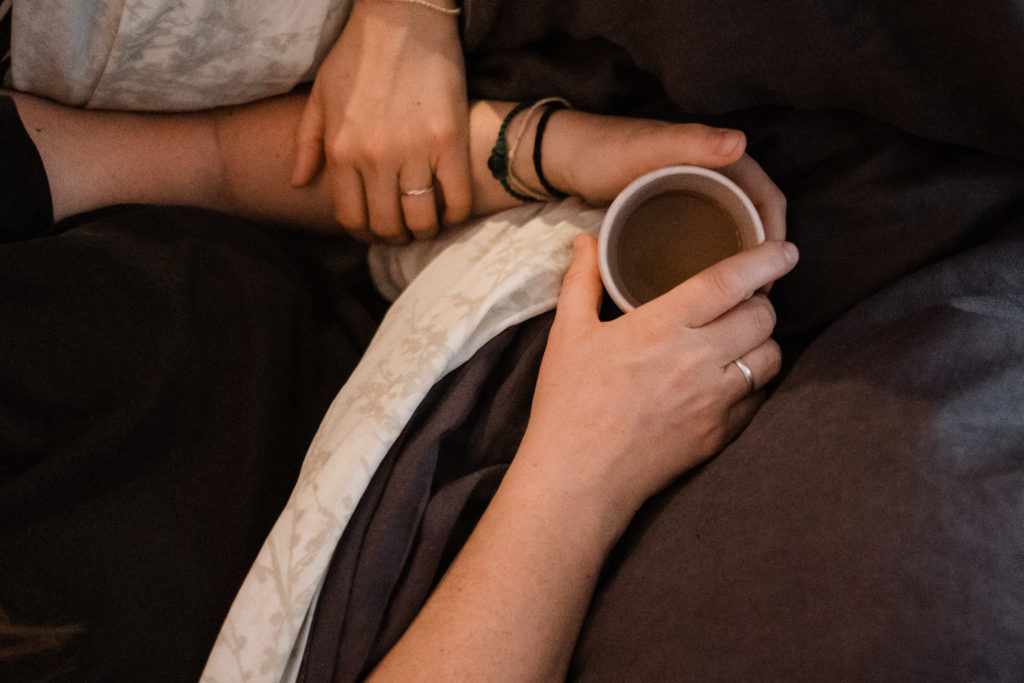 eine Frau hält eine Tasse in ihren Händen, eine andere Hand berührt ihren Arm