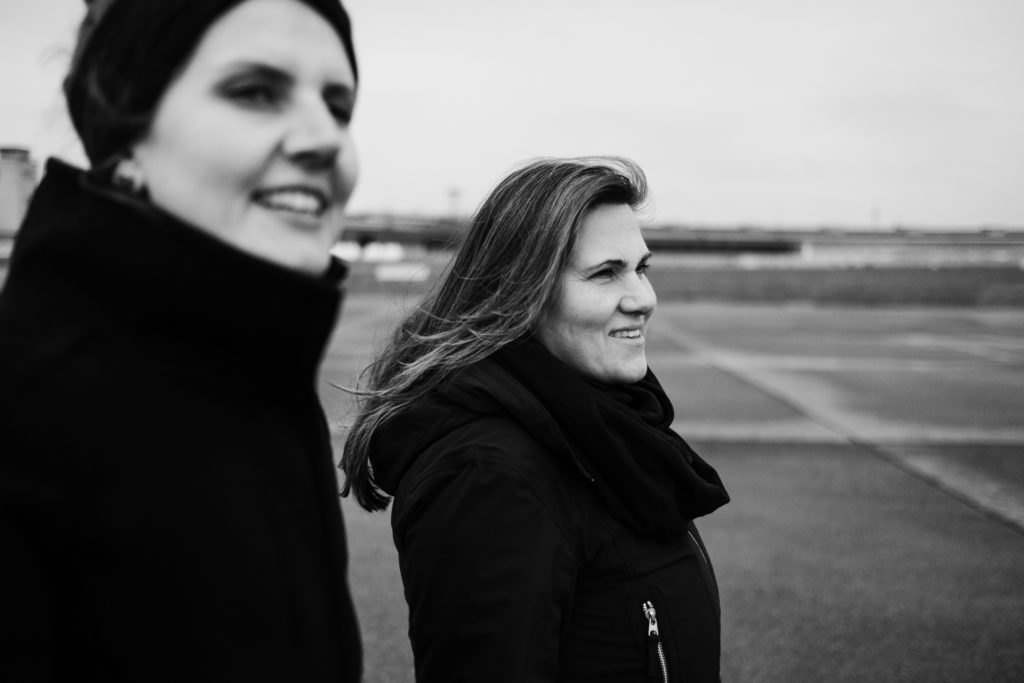 2 Frauen stehen auf dem Rollfeld des alten Flughafen in Berlin, sie sind beide schwarz gekleidet, sie blicken beide in die gleiche Richtung