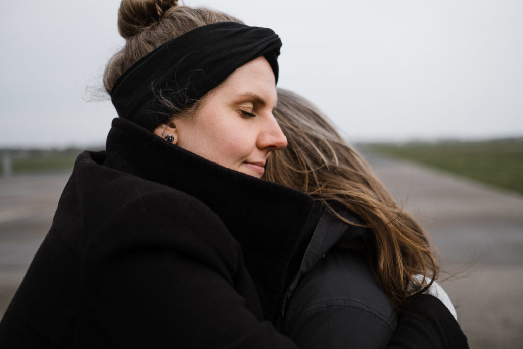 2 Frauen stehen auf dem Rollfeld des alten Flughafen in Berlin, sie sind beide schwarz gekleidet, sie umarmen sich und schließen dabei die Augen
