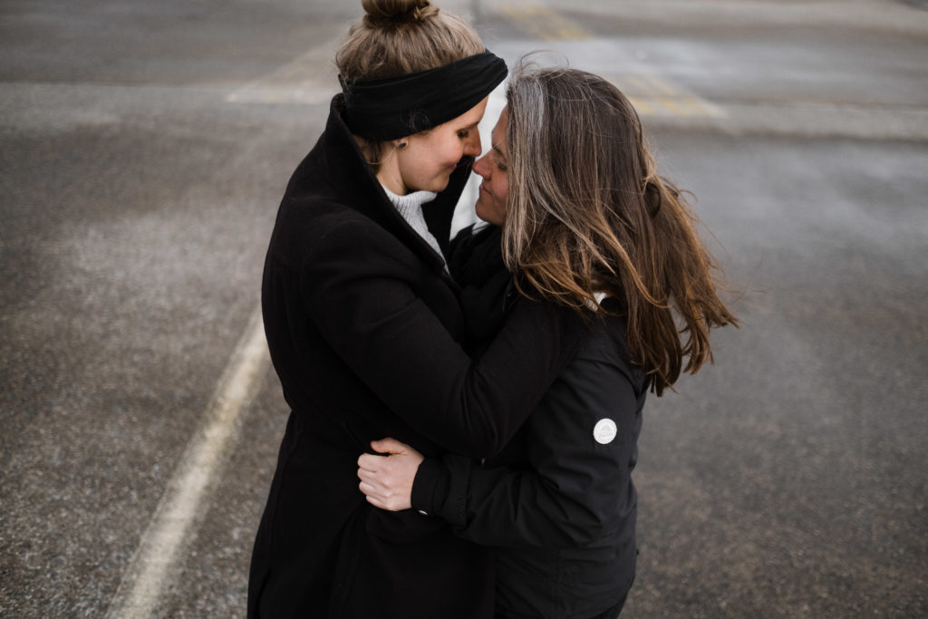 2 Frauen stehen auf dem Rollfeld des alten Flughafen in Berlin, sie sind beide schwarz gekleidet, sie umarmen sich, sie schauen sich in Gesicht