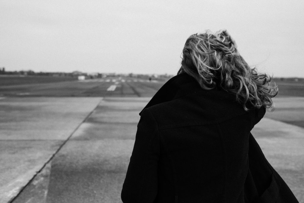 eine Frau steht auf dem Rollfeld des alten Flughafen in Berlin, sie schaut in die Ferne, der Wind weht durch ihr Haar, man sieht nur ihren Rücken