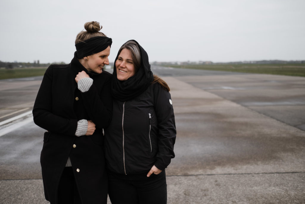 auf dem alten Rollfeld des Flughafen in Berlin stehen 2 Frauen nbeneinander, sie schauen sich gegnseitig an und lachen