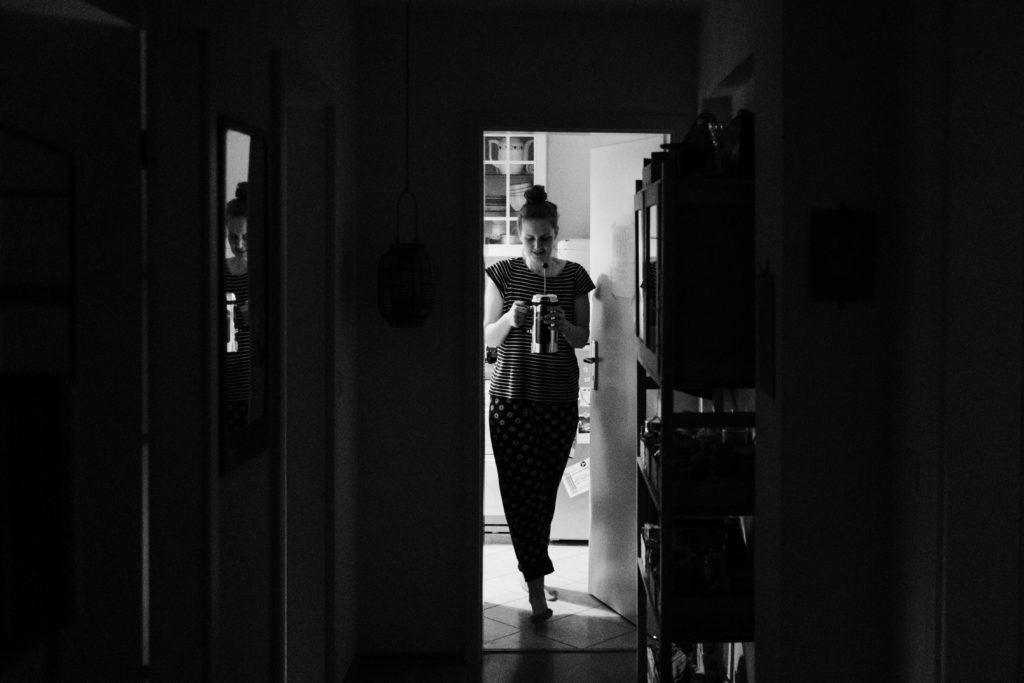 eine Frau kommt mit einer vollen Presskanne aus der Kuche in Richtung Flur, ihr Blick ist in Richtung Kanne gerichtet